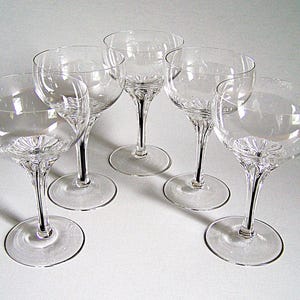 May include: A set of five clear glass stemmed coupes featuring a wide, rounded bowl and a short, faceted stem that transitions into a circular base. Each glass has a radial, sunburst-like pattern etched into the bottom of the bowl.