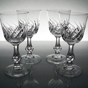 May include: A set of four clear crystal wine glasses featuring a cut glass pattern on the bowl and a faceted, diamond-shaped stem. Each glass has a circular base and a smooth, flared rim, showcasing intricate geometric engravings on the glass surface.