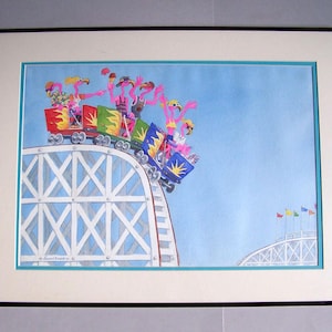 May include: A framed watercolor painting depicts pink flamingos riding a roller coaster. The coaster cars are colorful, and the track is white with blue accents. The background is a light blue sky with a few flags.