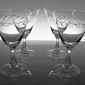 May include: Four clear crystal wine glasses with a diamond-shaped pattern around the rim. The glasses have a flared bowl, a slender stem, and a round base. The glasses are arranged in a symmetrical composition.