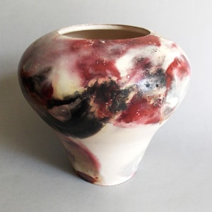 May include: A ceramic vase with a wide, rounded body and a narrow base, featuring a smooth, glazed surface. The exterior displays a marbled pattern of deep crimson, charcoal black, and creamy white tones, creating a swirling, abstract effect.