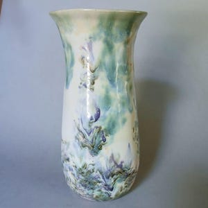May include: A ceramic vase with a flared rim and a smooth, glossy finish. The surface features a marbled, fluid pattern in shades of white, soft green, light blue, and hints of purple, creating a blended, watercolor-like appearance throughout.