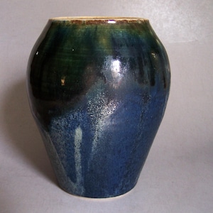 May include: A ceramic vase with a rounded body and a wide opening. The exterior features a glossy glaze that transitions from a deep forest green at the top to a vibrant royal blue at the base, with subtle white streaks and mottled textures.