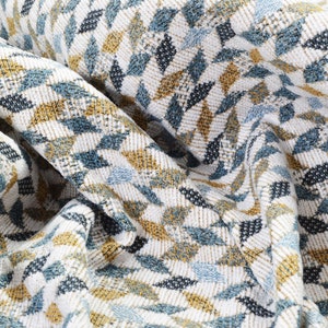 May include: Close-up of a white fabric with a geometric pattern in shades of blue and gold. The fabric is woven with a textured, slightly raised design.