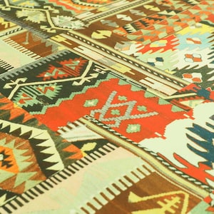 Può includere: Un tappeto patchwork colorato con motivi geometrici in tonalità di rosso, verde, blu e giallo. Il tappeto è realizzato in tessuto tessuto e ha un design tradizionale.