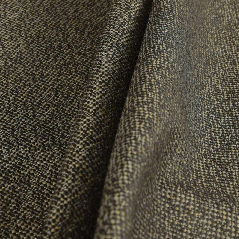 Puede incluir: Primer plano de una tela texturizada con un patr&oacute;n tejido. La tela tiene una mezcla de hilos gris oscuro, negros y beige, creando una apariencia moteada. El material est&aacute; doblado, mostrando profundidad y textura.