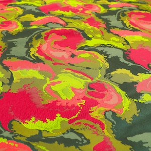 May include: Close-up of a fabric with a vibrant, abstract pattern. The design features swirling shapes in shades of hot pink, neon yellow, olive green, and dark gray. The fabric has a textured appearance, suggesting a woven or embroidered construction.