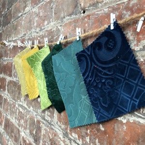 Può includere: Una collezione di campioni di tessuto in varie tonalità di verde e blu, con un campione di tessuto blu a fantasia alla fine. I campioni sono appesi a una corda con mollette.