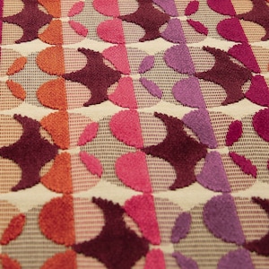 May include: A close-up of a fabric with a repeating pattern of overlapping circles in shades of pink, purple, orange, and brown. The fabric has a textured, almost fuzzy appearance.