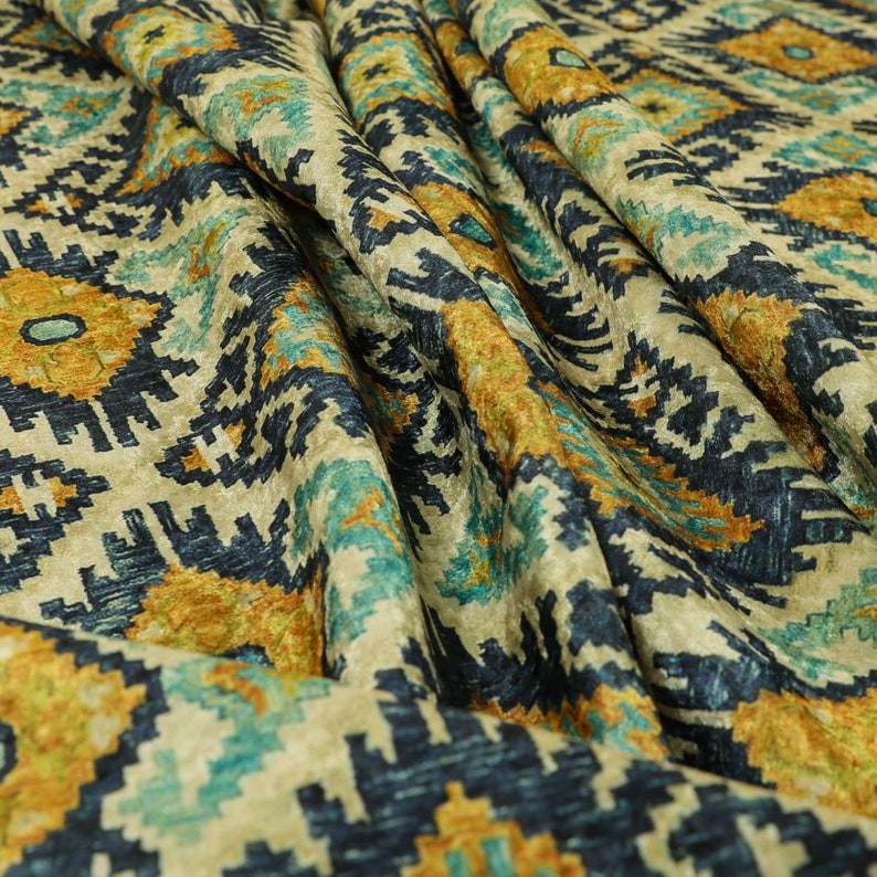 Op de afbeelding: Close-up van een stof met een geometrisch patroon in beige, blauwe en gouden tinten. De stof heeft een textuur en een geweven uitstraling.