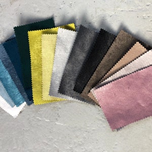 May include: A collection of fabric swatches in various colors, including teal, green, yellow, gray, black, brown, beige, and pink. The swatches are arranged in a fan shape, with the pink swatch at the bottom.