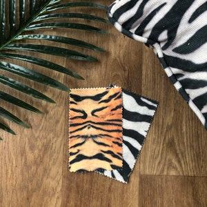 May include: Two fabric swatches, one with a tiger print and the other with a zebra print. The tiger print is orange, black, and white. The zebra print is black and white.