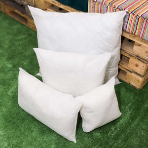 May include: Four white pillows of different sizes stacked on top of each other on a green artificial grass surface.