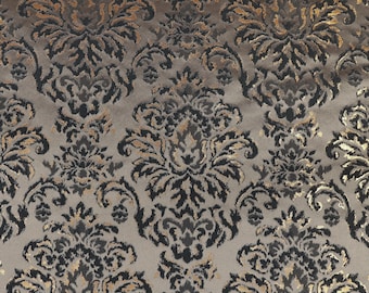 May include: A close-up of a fabric with a repeating damask pattern. The fabric features a muted gray background with ornate floral designs in black, gold, and darker gray tones. The pattern is detailed and creates a luxurious texture.