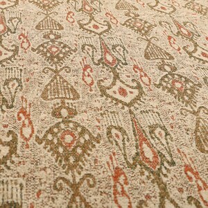 May include: Close-up of a beige fabric with a repeating pattern in shades of brown and rust. The design features stylized shapes and geometric elements, creating a textured, vintage aesthetic. The fabric appears to be woven, suggesting a textile product.