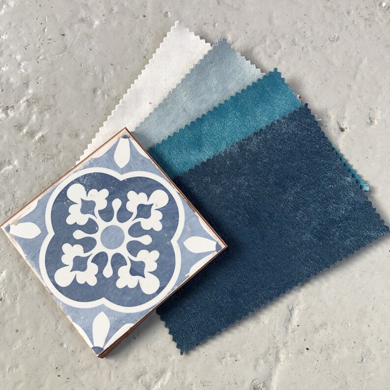 May include: A collection of fabric swatches in shades of blue, teal, and white. The swatches are arranged in a fan shape, with the darkest blue at the bottom and the lightest white at the top. The swatches are placed on a light gray surface.