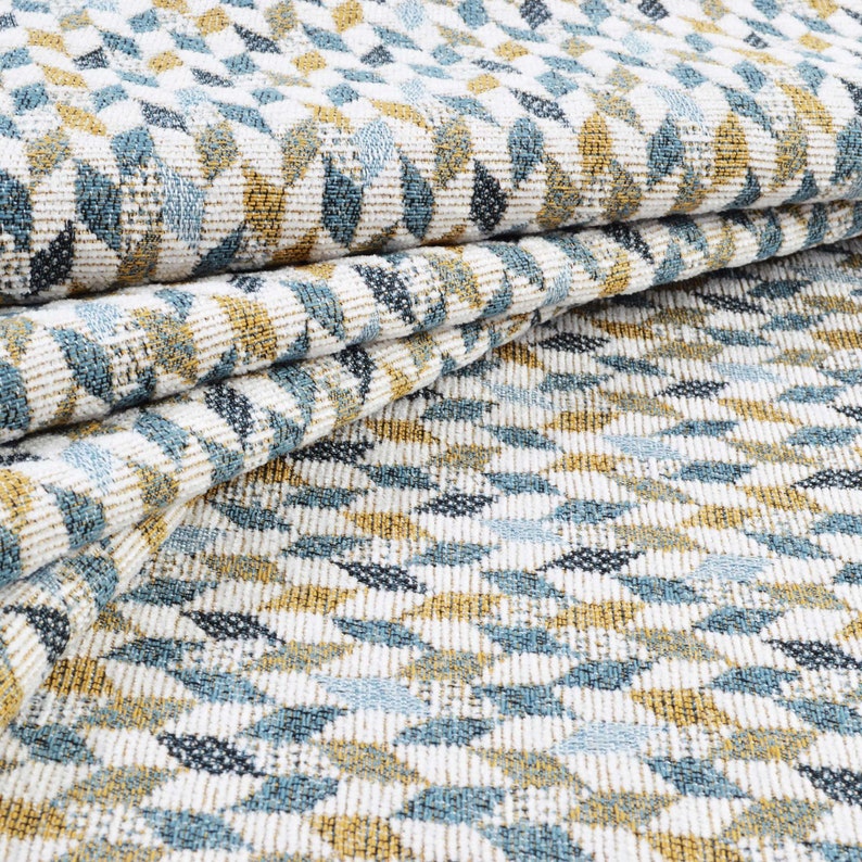 May include: Close-up of a white fabric with a geometric pattern of blue and gold leaves. The fabric is folded in half, showing the pattern on both sides.