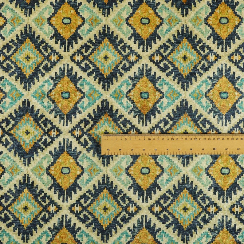 Op de afbeelding: Een stofstaal met een herhalend geometrisch patroon in tinten blauw, geel en wit. De stof heeft een textuur en een geweven uitstraling.
