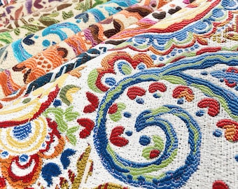 May include: A close-up of colorful fabric with a paisley pattern. The fabric is white with blue, red, green, and yellow accents. The fabric is woven with a textured surface.