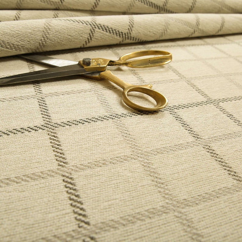 May include: A pair of gold scissors with a silver blade lying on a beige fabric with a black and white geometric pattern.