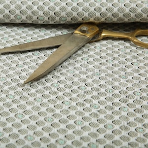 Puede incluir: Un par de tijeras con mangos dorados y cuchillas plateadas que descansan sobre una tela blanca con un patrón hexagonal repetitivo.