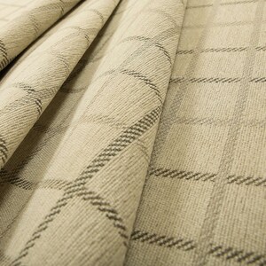 May include: Beige fabric with a subtle black and white plaid pattern. The fabric is folded and textured.