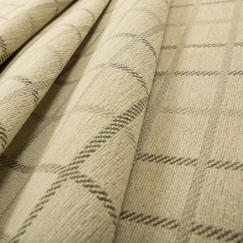 May include: Beige fabric with a subtle black and white plaid pattern. The fabric is folded and textured.