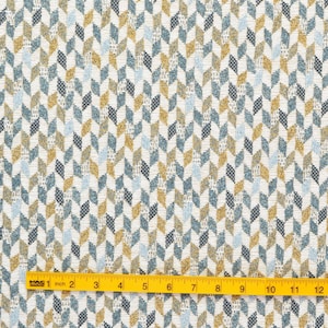 May include: A white fabric with a geometric pattern of blue, yellow, and grey chevron shapes. The fabric is measured with a yellow ruler.