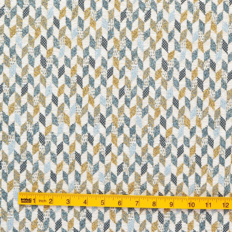 May include: A white fabric with a geometric pattern of blue, yellow, and grey chevron shapes. The fabric is measured with a yellow ruler.