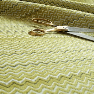 May include: A close-up of a green and white chevron patterned fabric with a pair of gold scissors on top.