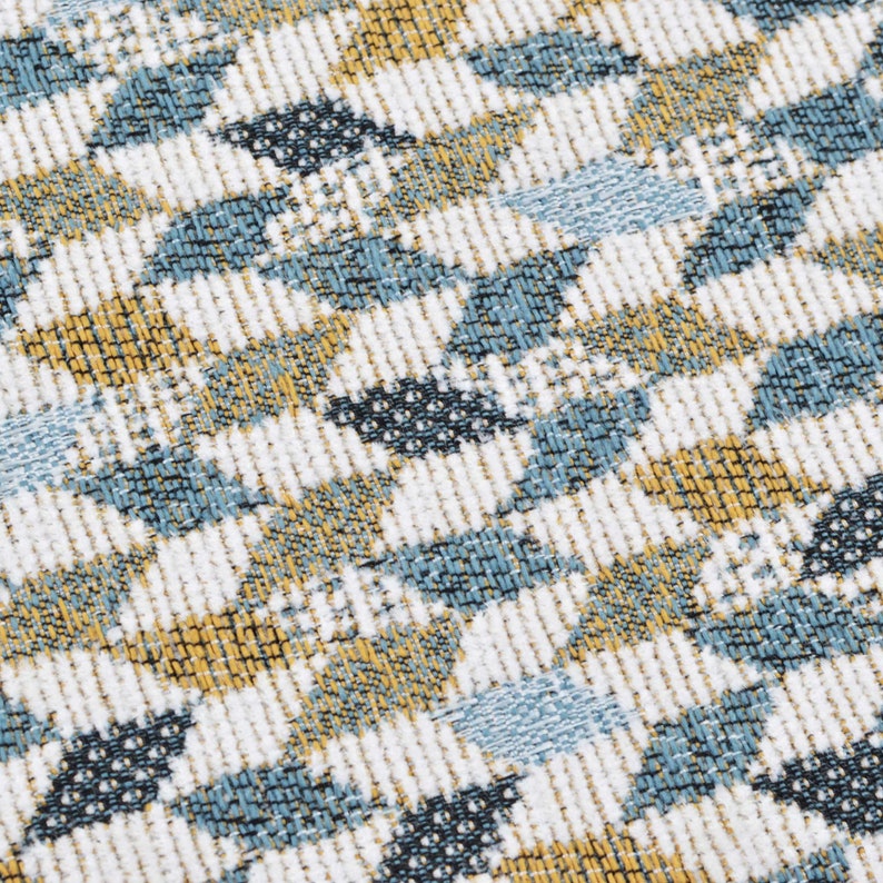 May include: A close-up of a fabric with a repeating pattern of blue, white and yellow geometric shapes. The fabric has a textured surface.
