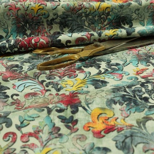 May include: A close-up of a fabric with a colorful floral pattern. The fabric is a light green color with a variety of blue, red, yellow, and orange flowers. A pair of scissors is lying on top of the fabric.
