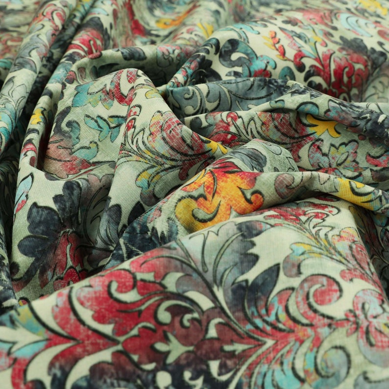 May include: A close-up of a fabric with a colorful floral pattern. The fabric is a light green color with a variety of shades of blue, red, yellow, and orange. The flowers are stylized and have a vintage look.