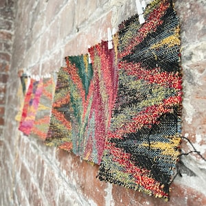May include: A collection of colorful fabric swatches with geometric patterns, displayed on a brick wall. The swatches are arranged in a row, with the most prominent one featuring a black, red, and gold design.