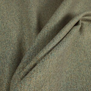 Puede incluir: Primer plano de una tela texturizada con tonos verdes, azules y beige. El material est&aacute; doblado, revelando el tejido y las variaciones de color. La tela parece ser de peso medio, adecuada para tapicer&iacute;a o cortinas.