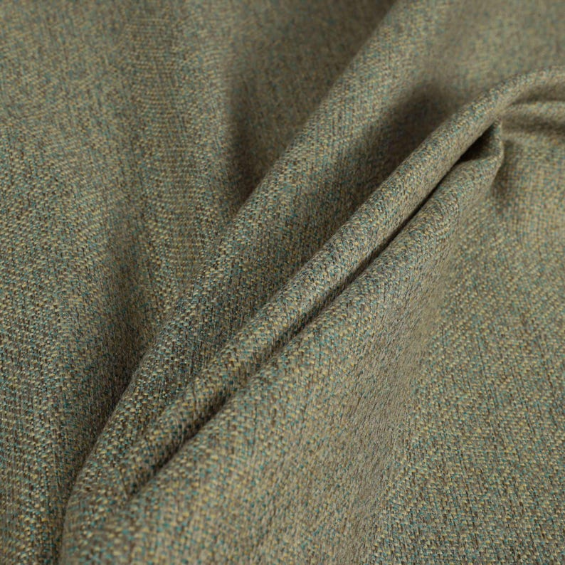 Puede incluir: Primer plano de una tela texturizada con tonos verdes, azules y beige. El material est&aacute; doblado, revelando el tejido y las variaciones de color. La tela parece ser de peso medio, adecuada para tapicer&iacute;a o cortinas.