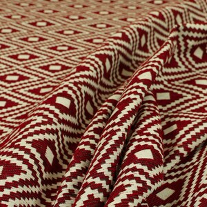 May include: Red and white geometric patterned fabric with a woven texture. The fabric is folded and draped, showing the pattern and texture.
