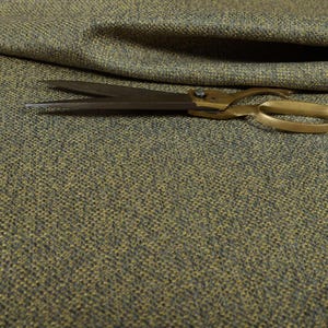 Puede incluir: Primer plano de tela texturizada en tonos verde oliva y gris. Un par de tijeras antiguas de lat&oacute;n descansa sobre la tela. La tela parece ser un material tejido, posiblemente para tapicer&iacute;a o cortinas. Las tijeras est&aacute;n abiertas.
