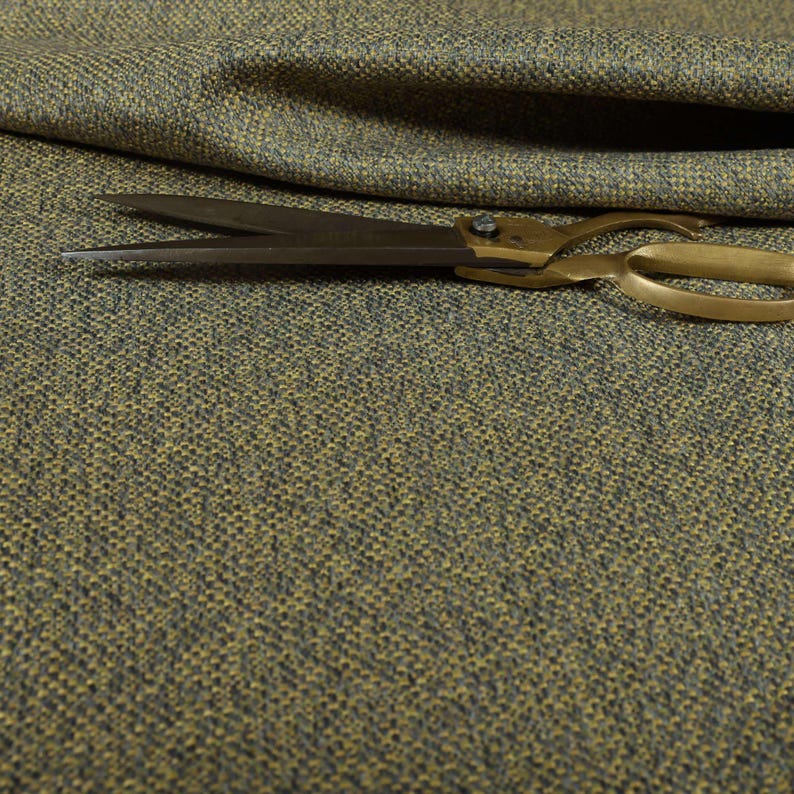 Puede incluir: Primer plano de tela texturizada en tonos verde oliva y gris. Un par de tijeras antiguas de lat&oacute;n descansa sobre la tela. La tela parece ser un material tejido, posiblemente para tapicer&iacute;a o cortinas. Las tijeras est&aacute;n abiertas.