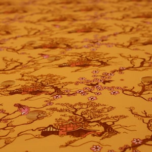 Può includere: Primo piano di un tessuto con un motivo ripetuto di alberi, edifici e fiori in stile giapponese nei toni del marrone, rosa e arancione. Il design ha un'estetica vintage, con una messa a fuoco leggermente sfocata.