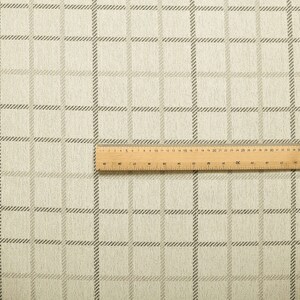 May include: A close-up of a beige fabric with a subtle brown plaid pattern. The fabric is textured and has a slightly rough feel.