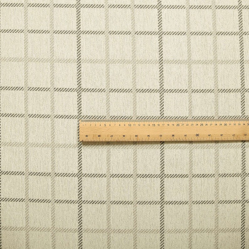 May include: A close-up of a beige fabric with a subtle brown plaid pattern. The fabric is textured and has a slightly rough feel.