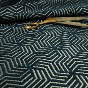 May include: A close-up shot of teal fabric featuring a geometric pattern of white lines. A pair of gold-coloured scissors lies on the fabric, partially covering the design. The fabric has a textured appearance, possibly woven or embroidered.