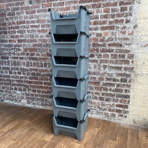 May include: A stack of six grey plastic storage bins with black handles. The bins are stacked on top of each other and are in a vertical position.