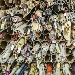 May include: A wall filled with rolls of fabric in various colors and patterns, stored in cardboard tubes. The fabric rolls are organized in rows and columns, creating a visually appealing display.