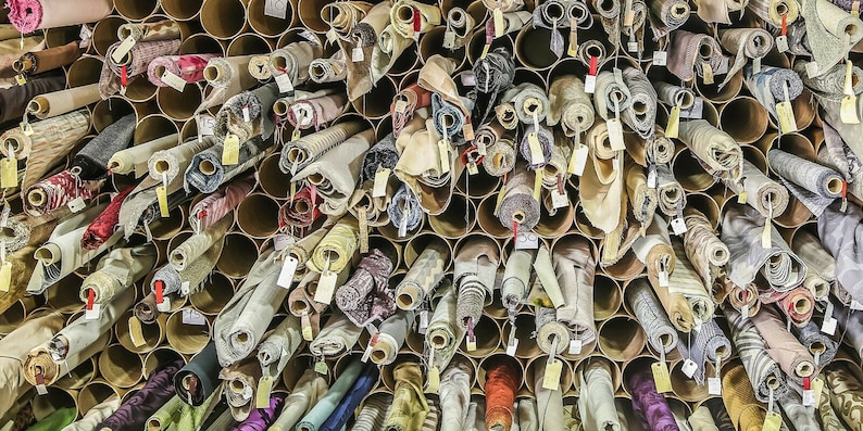 May include: A wall filled with rolls of fabric in various colors and patterns, stored in cardboard tubes. The fabric rolls are organized in rows and columns, creating a visually appealing display.