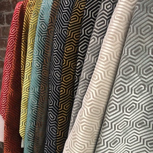 May include: A collection of fabric swatches featuring geometric patterns in various colours, including red, yellow, blue, black, gold, and grey. The patterns are all similar, featuring a repeating hexagonal design.