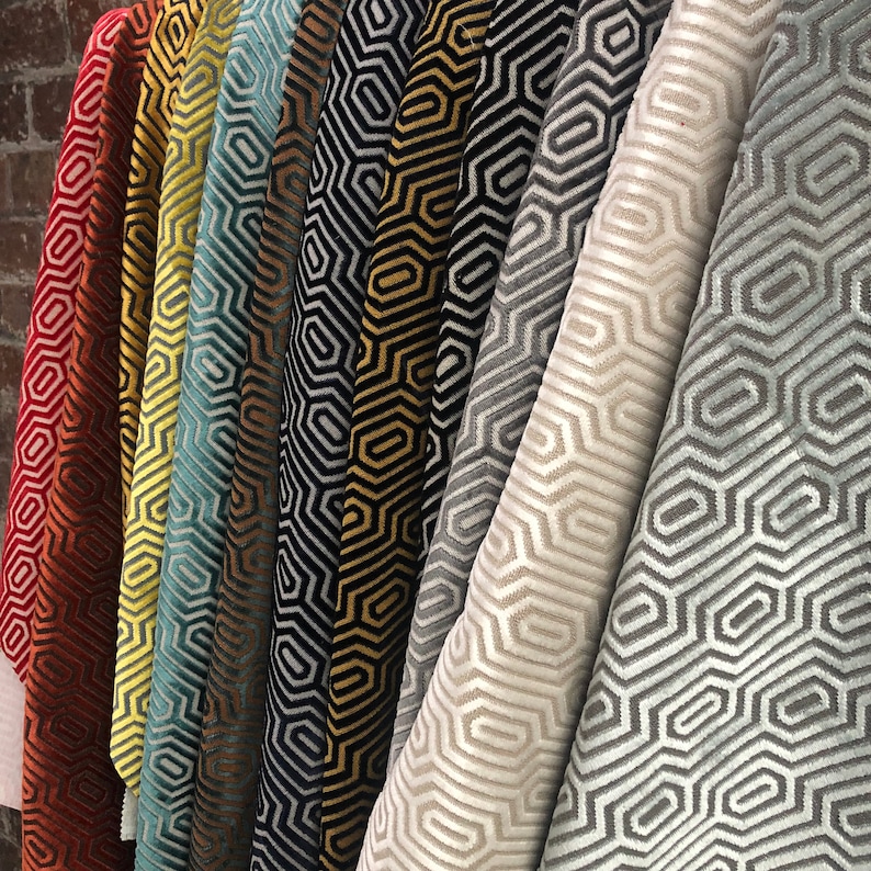 May include: A collection of fabric swatches featuring geometric patterns in various colours, including red, yellow, blue, black, gold, and grey. The patterns are all similar, featuring a repeating hexagonal design.