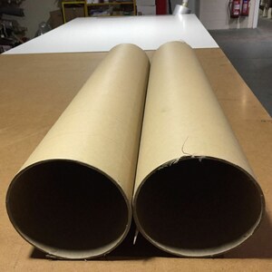 May include: Two large brown cardboard tubes, lying side by side on a wooden surface.