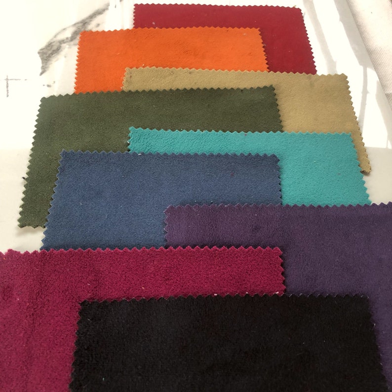 May include: A collection of fabric swatches in various colors, including red, orange, brown, green, teal, blue, purple, burgundy, and black. The fabric swatches are arranged in a stack, with the darkest color at the bottom and the lightest color at the top.